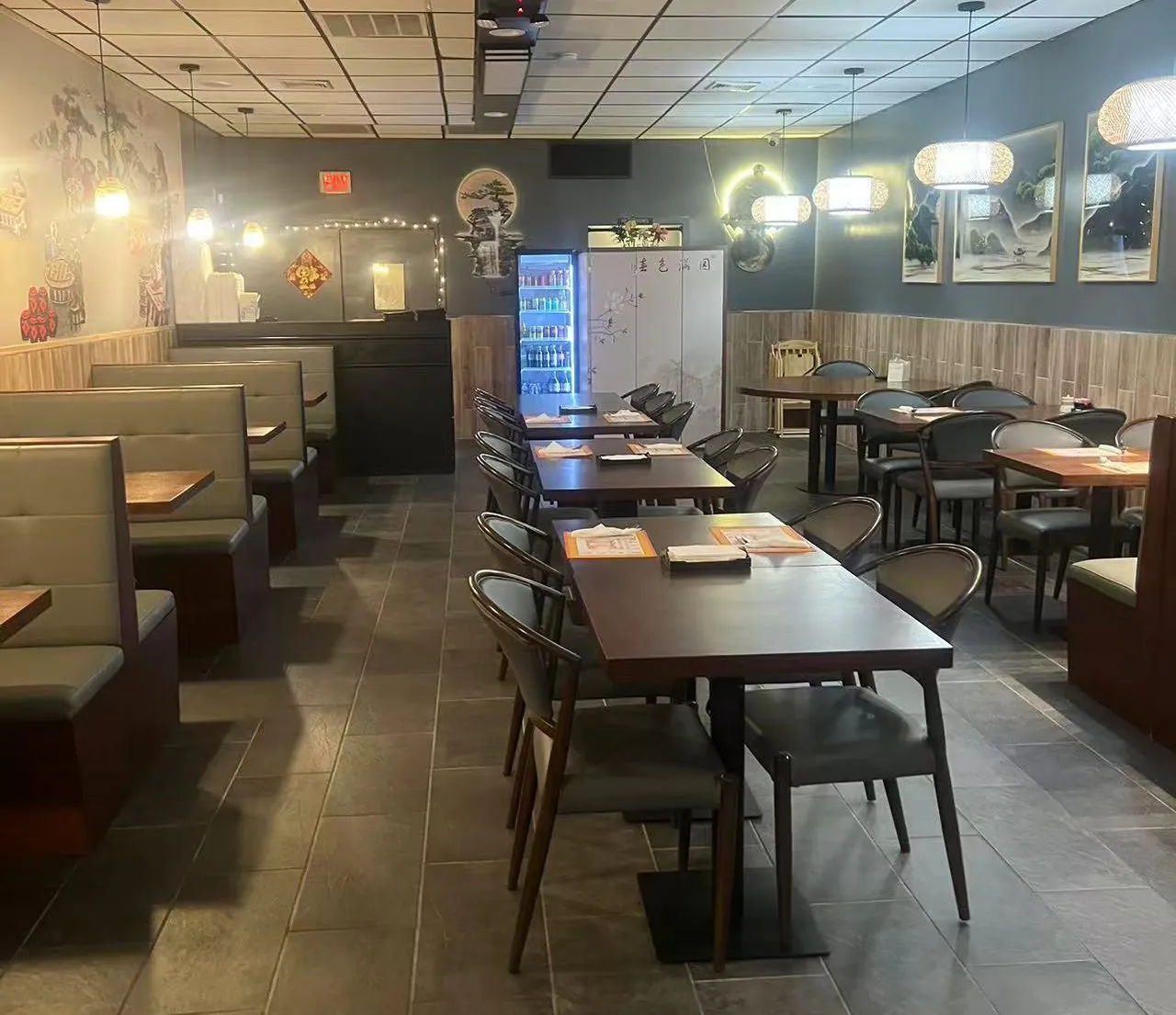 The interior of a restaurant with dark tiled floors, wooden tables, cushioned booths, and Asian-inspired wall art and lighting.